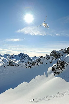 Heli fliegt über Lech die Piste-drei Ski tourengeher erklimmen den Berg