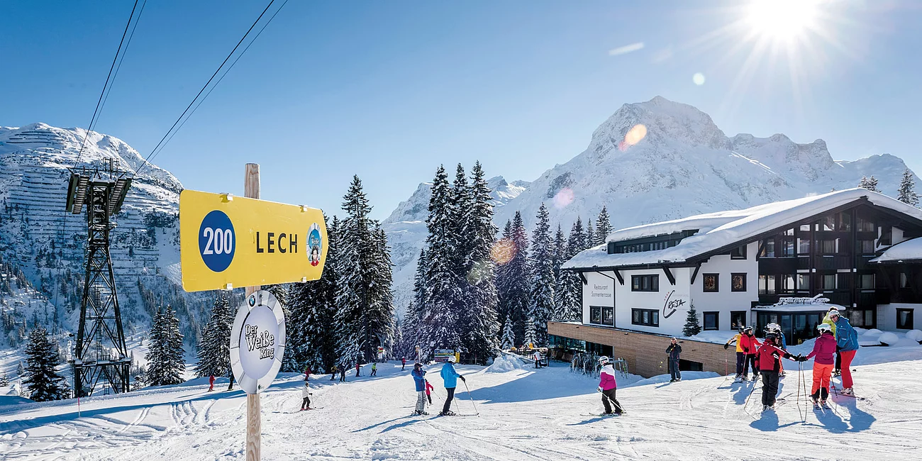 Pistennummernschild, Skifahrer und im Hintergrund das Hotl