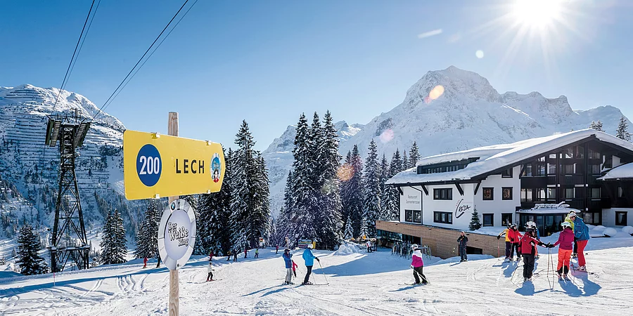 Pistennummernschild, Skifahrer und im Hintergrund das Hotl